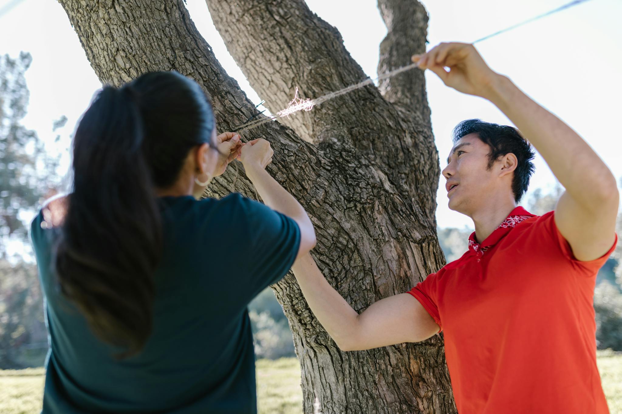 Two adults collaborating in a team building exercise outdoors, tying rope on a tree.